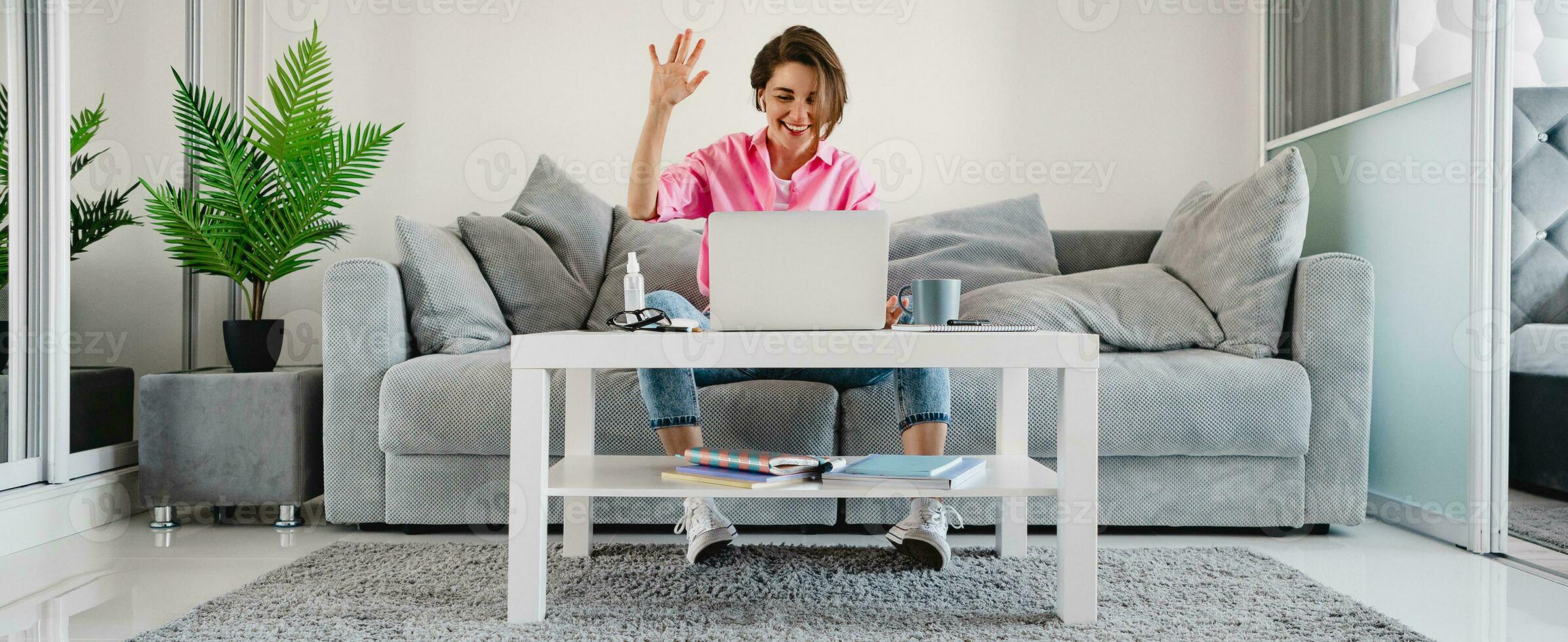 woman in pink shirt sitting relaxed on sofa at home at table working online on laptop photo