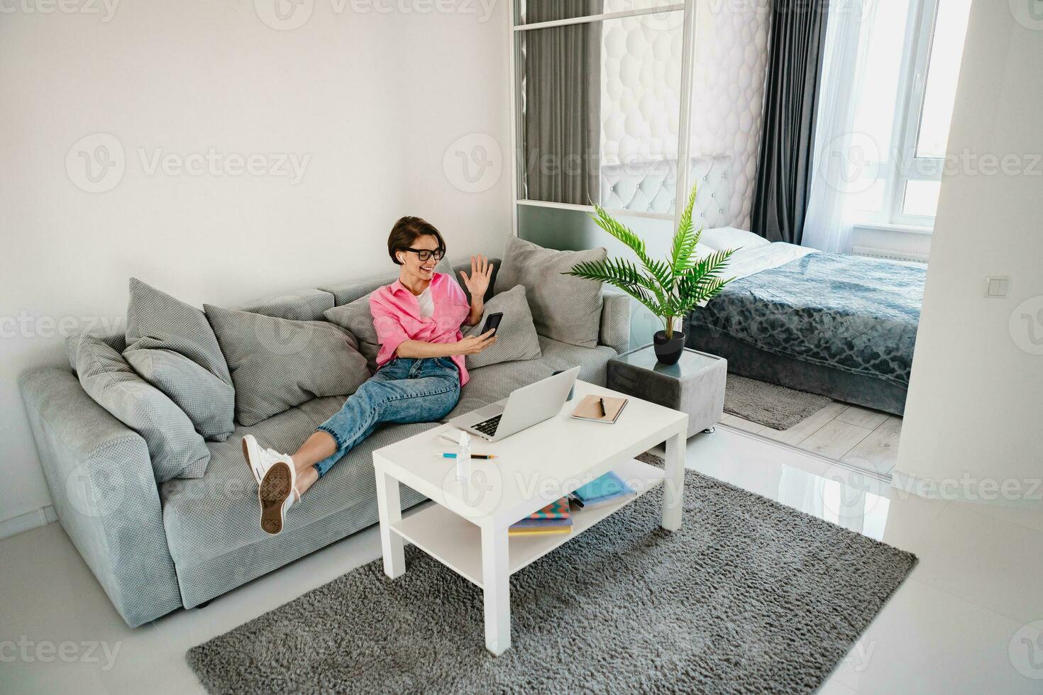 attractive smiling woman in pink shirt sitting relaxed on sofa at home photo