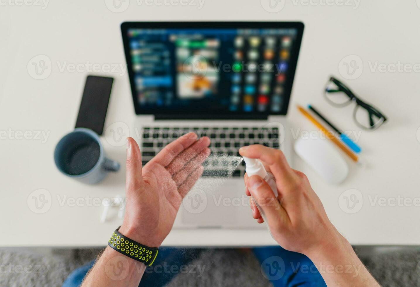 view from above on table close-up man cleaning hands with sanitizer antiseptic spray at workplace photo