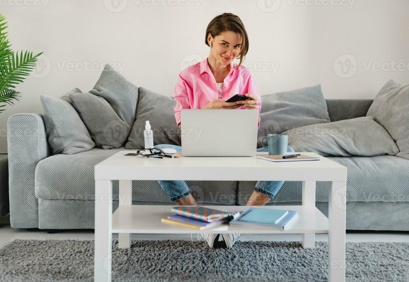 woman in pink shirt sitting relaxed on sofa at home at table working online on laptop photo