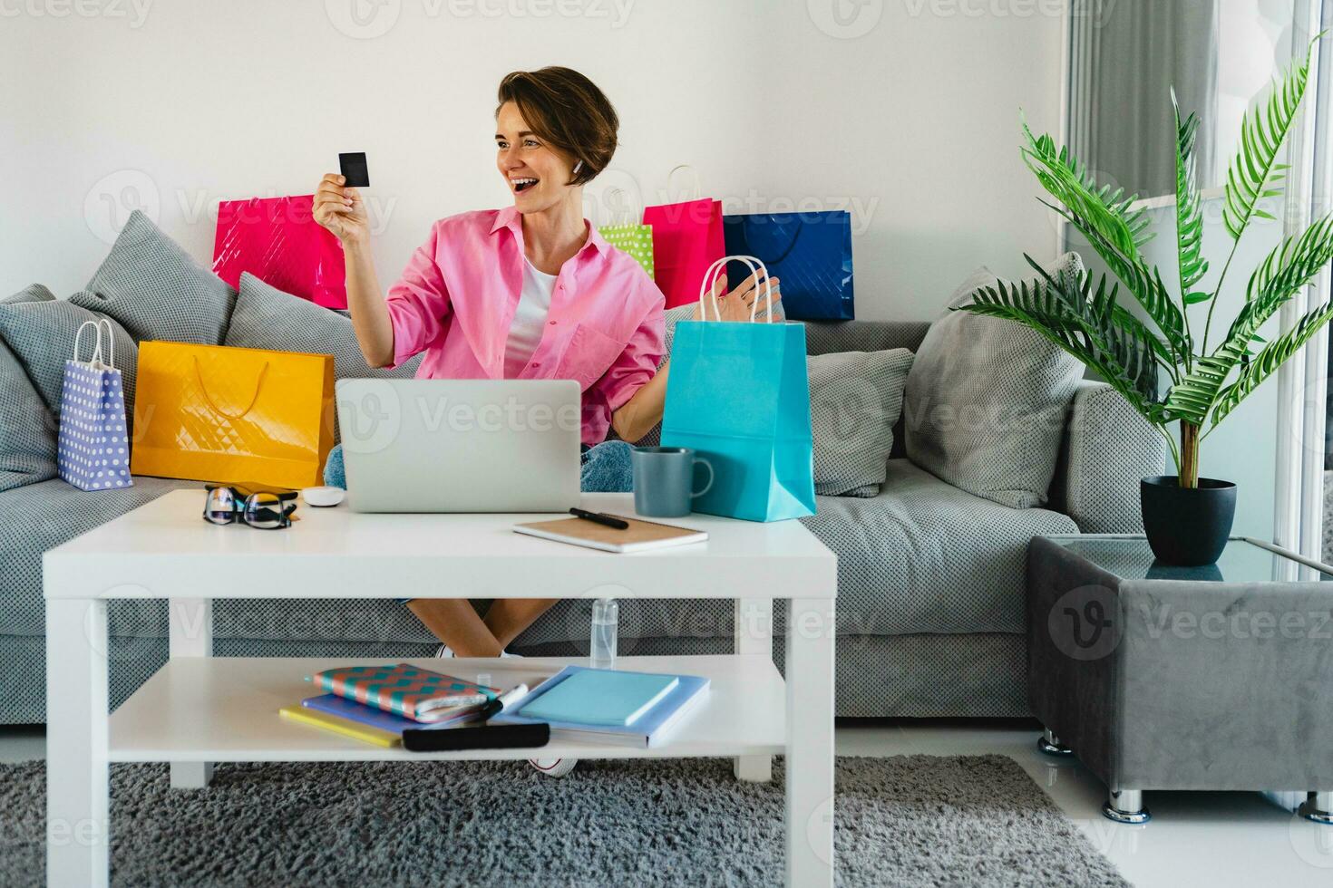 happy smiling woman in pink shirt on sofa at home shopping online photo