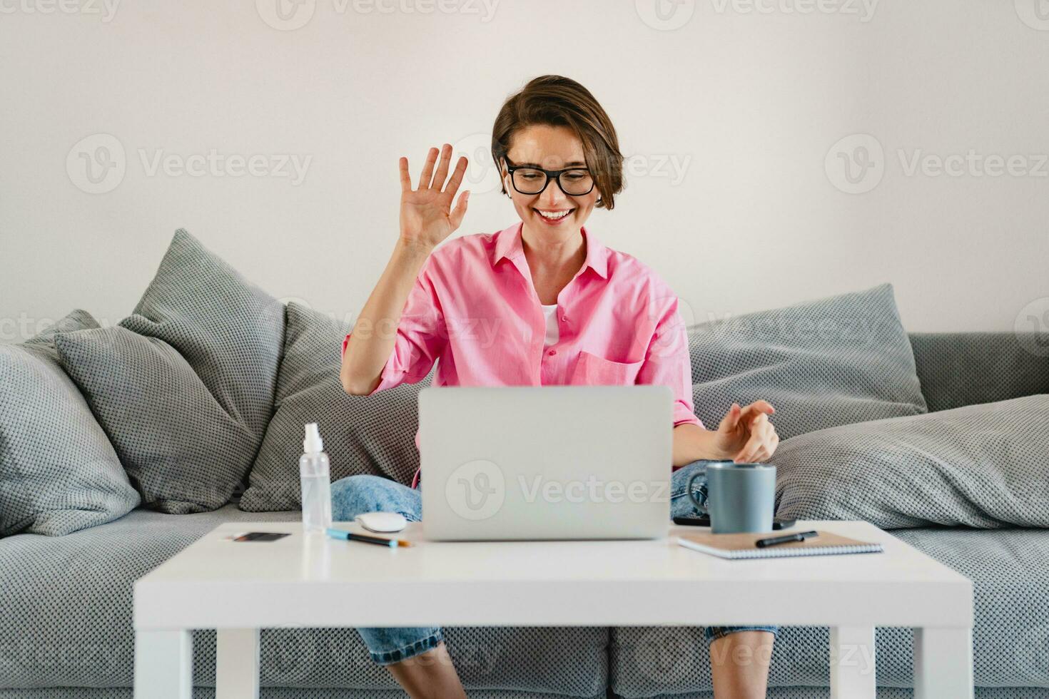 woman in pink shirt sitting relaxed on sofa at home at table working online on laptop photo