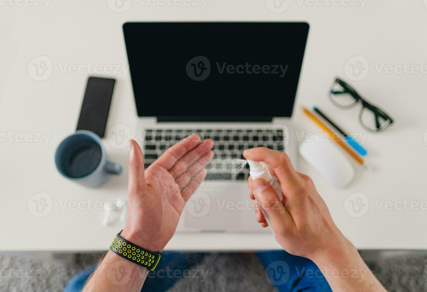 view from above on table close-up man cleaning hands with sanitizer antiseptic spray at workplace photo
