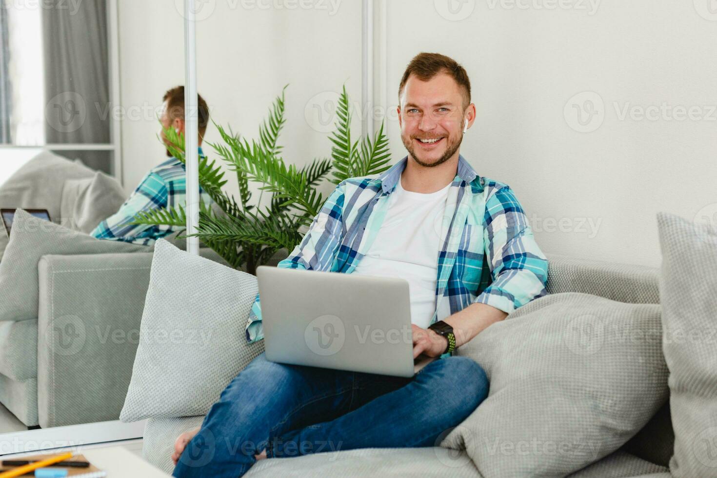 handsome smiling man in shirt sitting relaxed on sofa at home at table working online on laptop photo