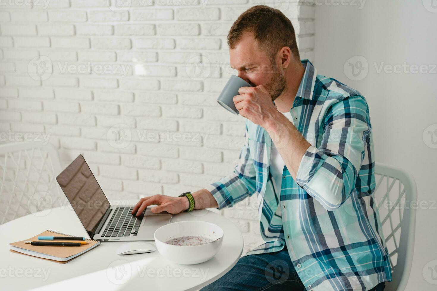 man in shirt sitting in kitchen at home at table working online on laptop photo