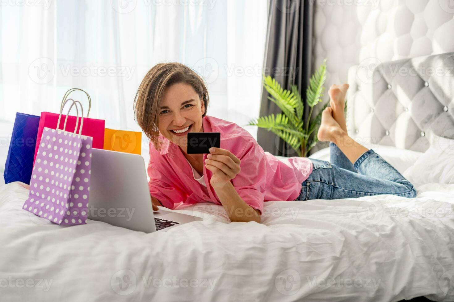 pretty happy woman lying on bed at home shopping online photo