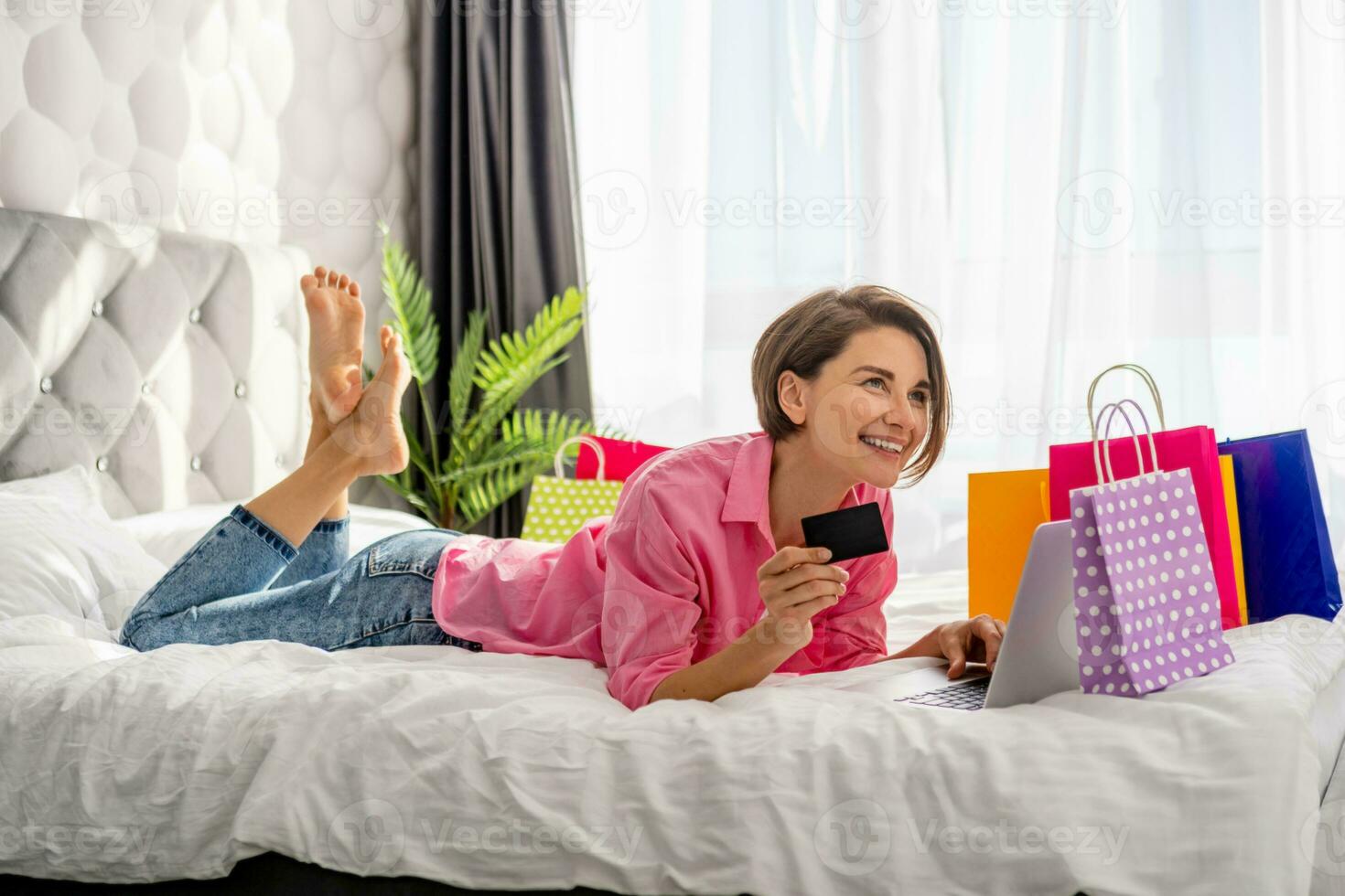pretty happy woman lying on bed at home shopping online photo