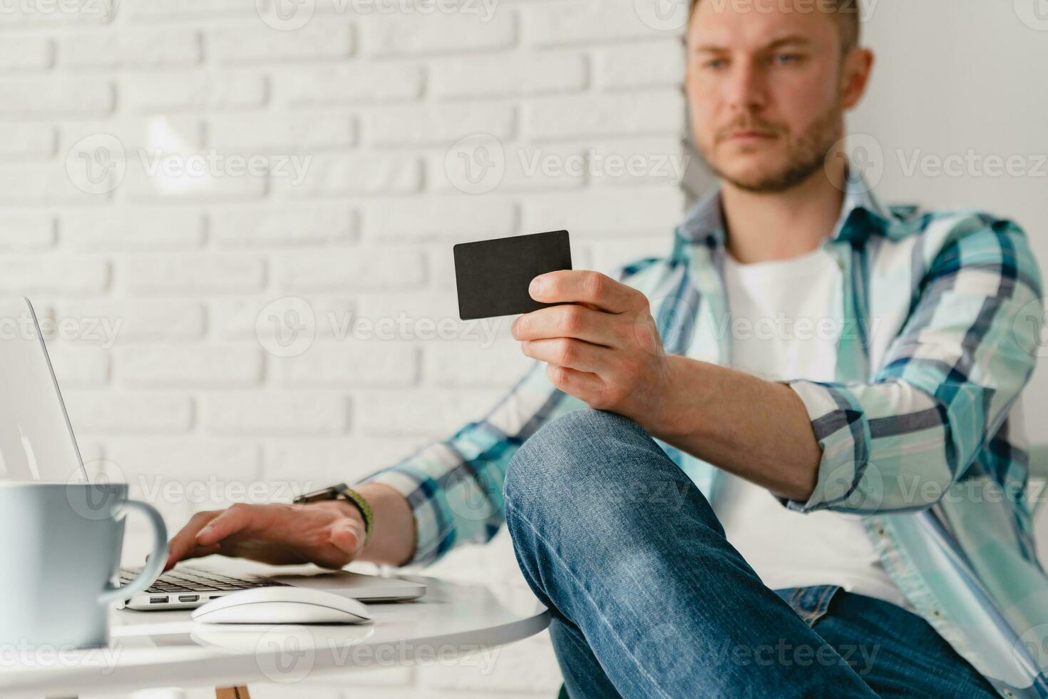 handsome smiling man in shirt sitting in kitchen at home at table working online on laptop photo