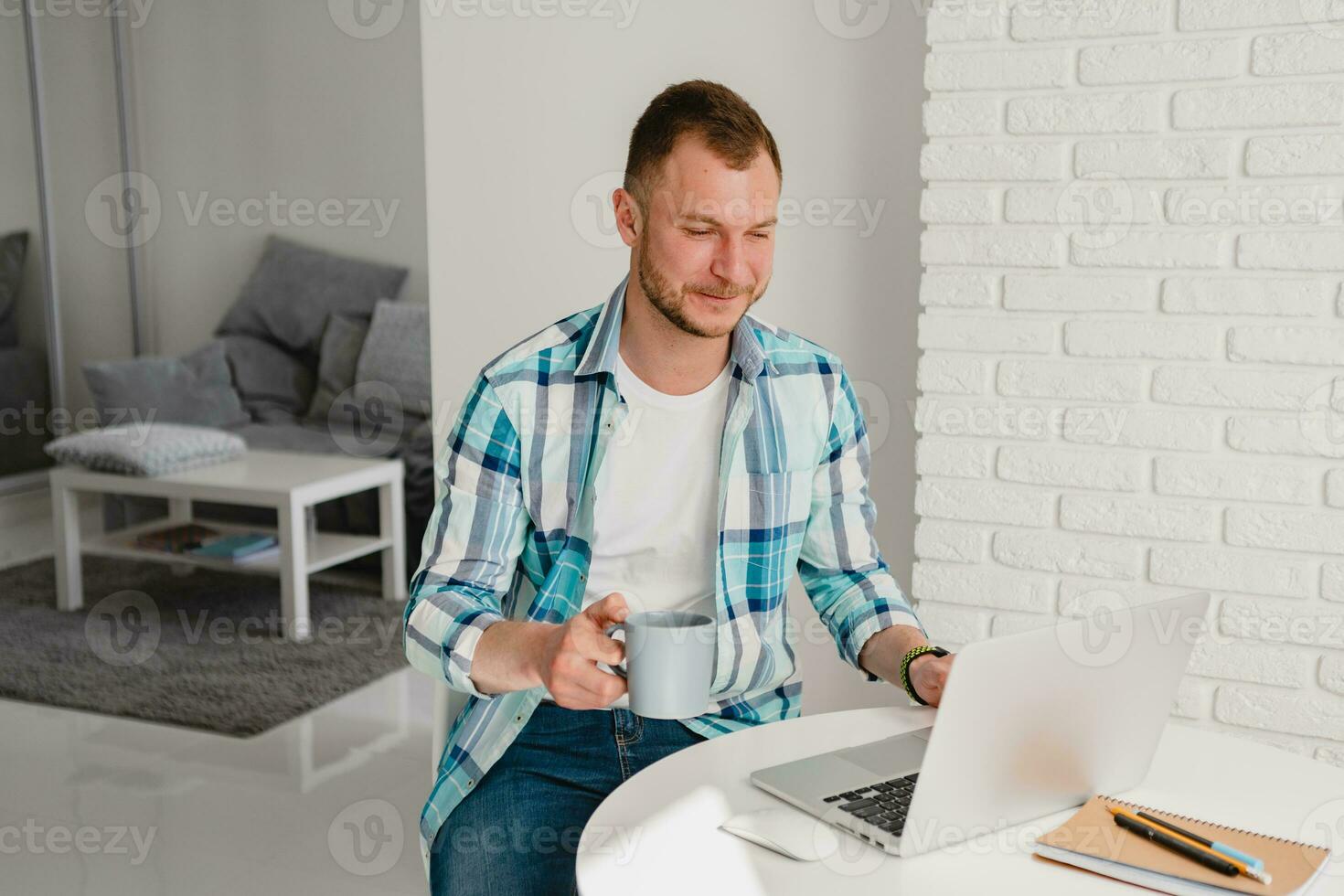 handsome smiling man in shirt sitting in kitchen at home at table working online on laptop photo