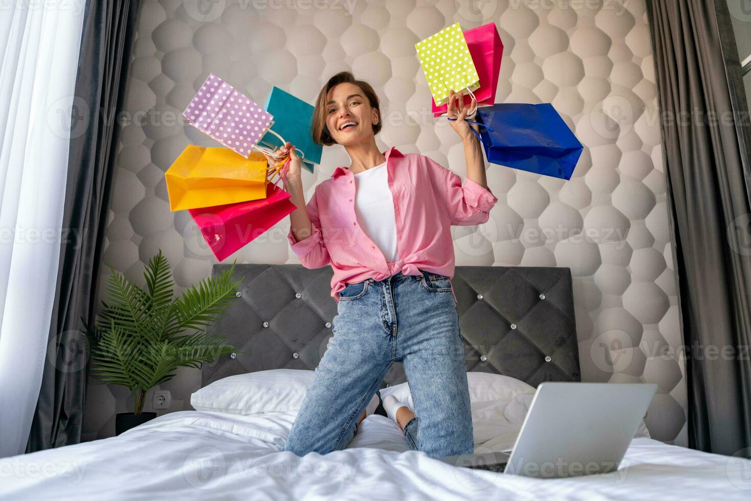 pretty happy woman jumping on bed at home shopping online photo