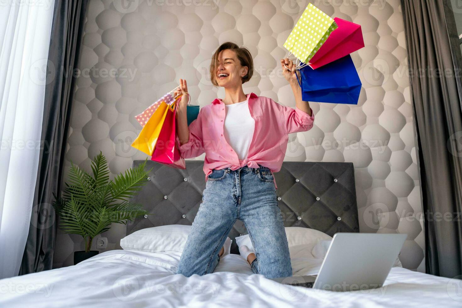 pretty happy woman jumping on bed at home shopping online photo