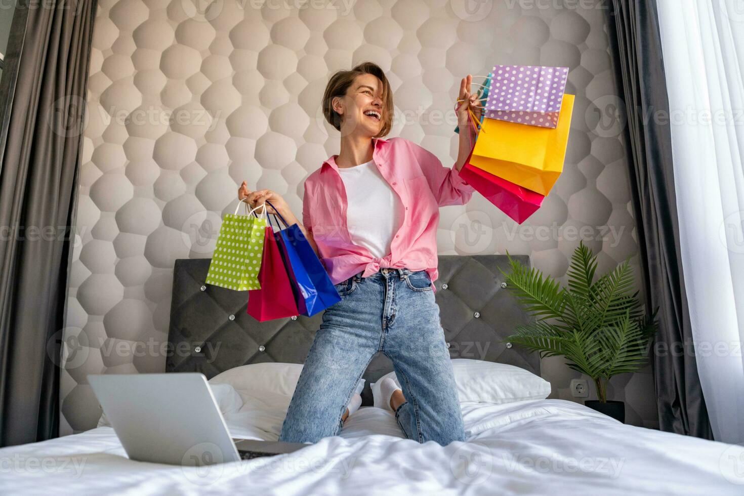 pretty happy woman jumping on bed at home shopping online photo