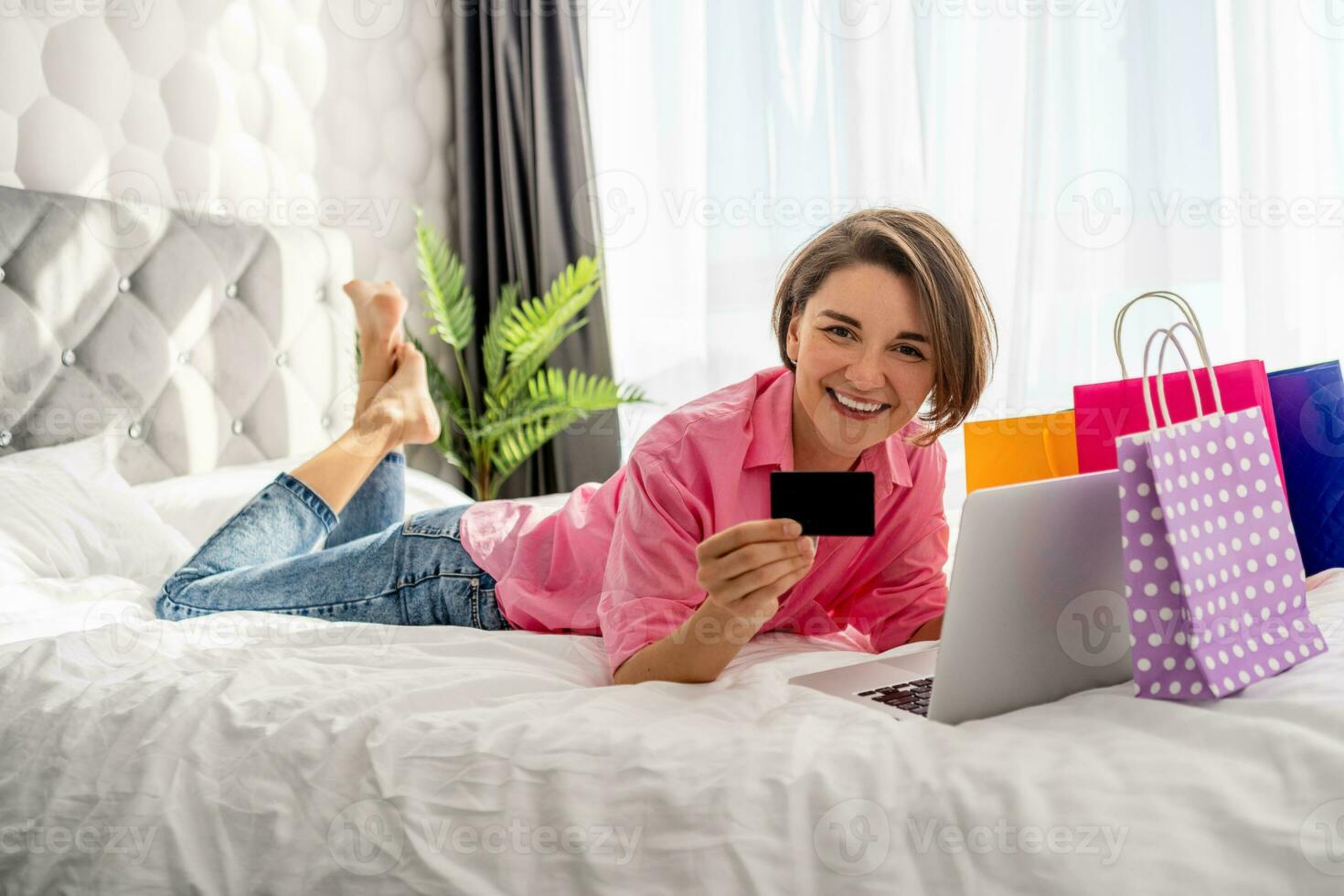 pretty happy woman lying on bed at home shoppping online photo