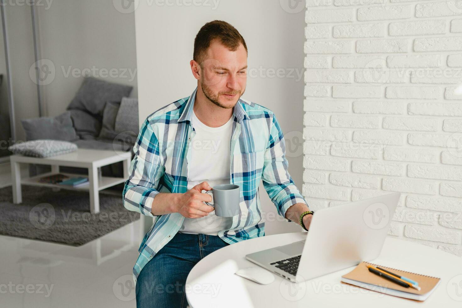 handsome smiling man in shirt sitting in kitchen at home at table working online on laptop photo