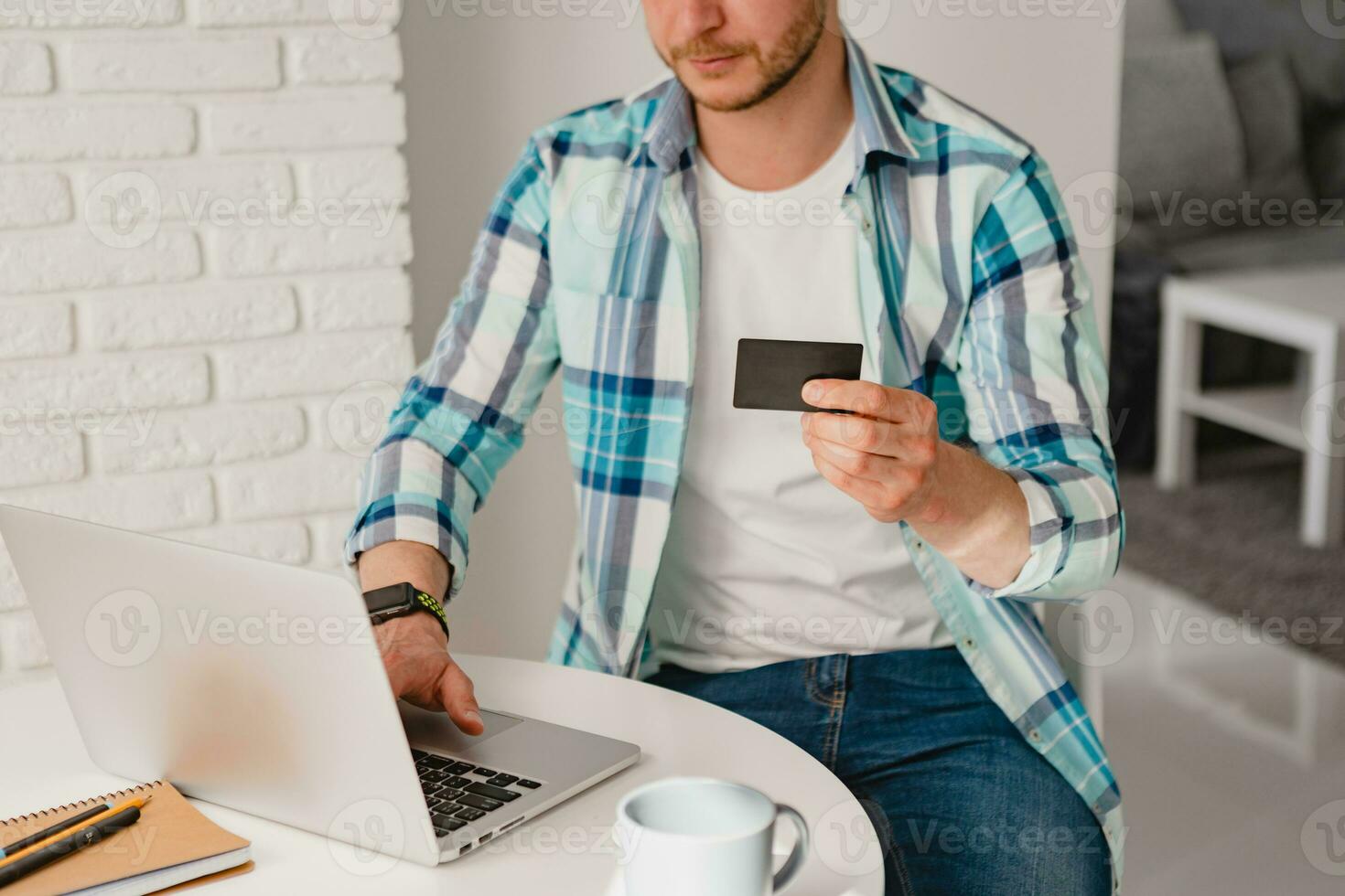 handsome smiling man in shirt sitting in kitchen at home at table working online on laptop photo