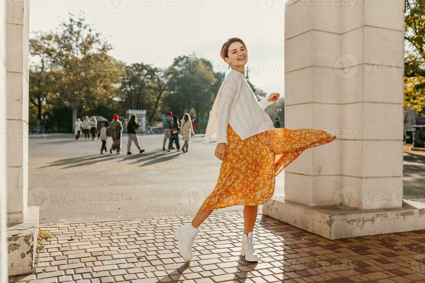 young pretty happy smiling woman in yellow printed dress and knitted white sweater photo