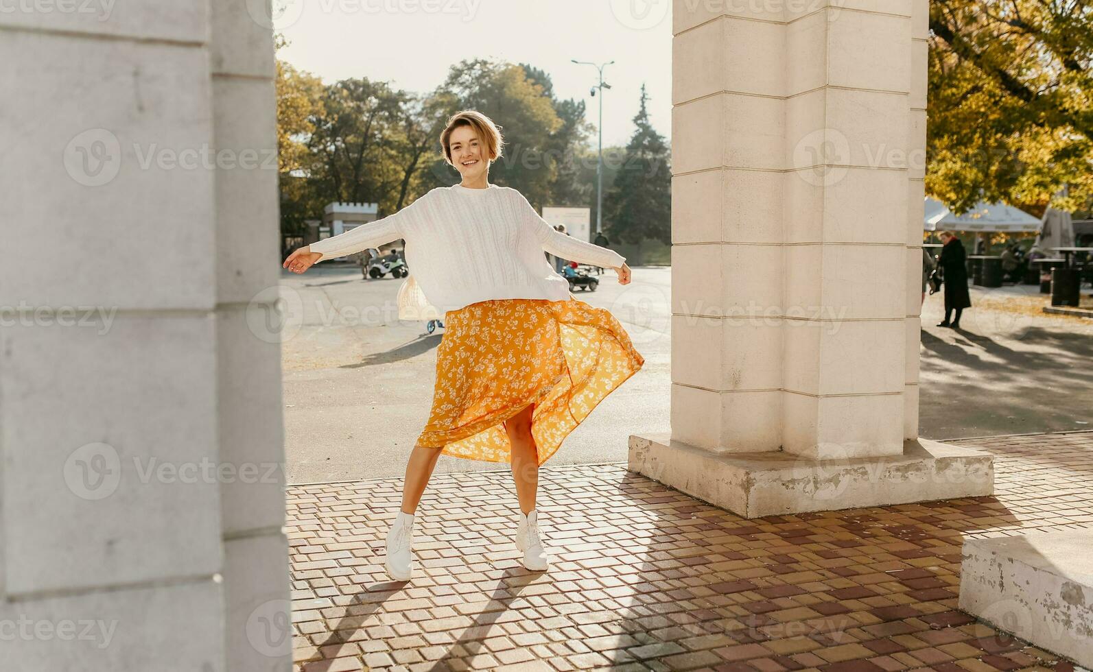 young pretty happy smiling woman in yellow printed dress and knitted white sweater photo