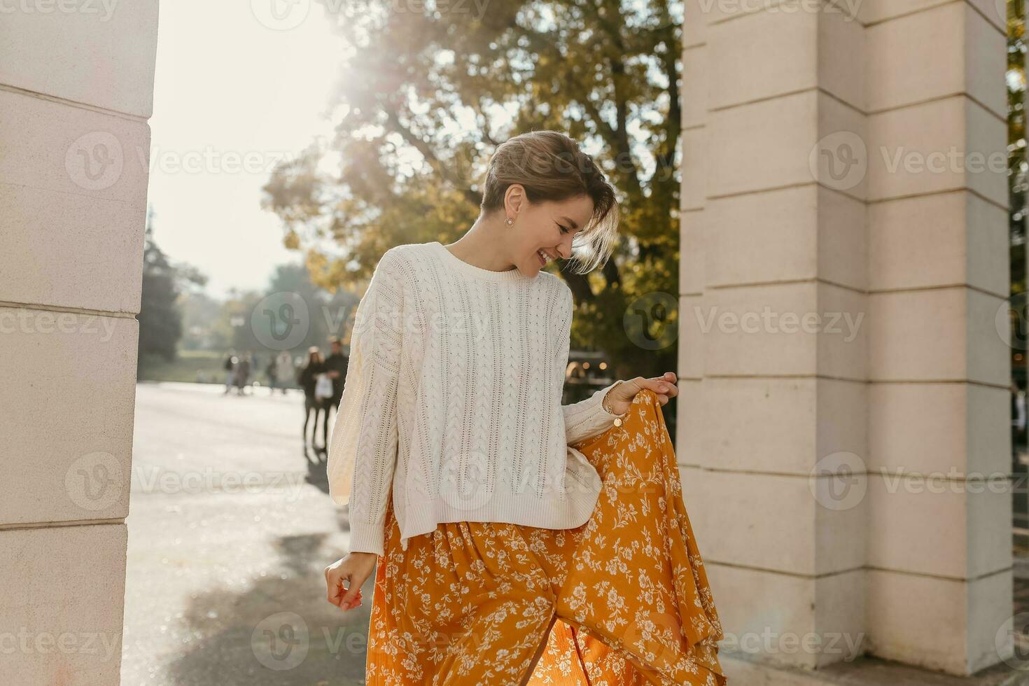 young pretty happy smiling woman in yellow printed dress and knitted white sweater photo