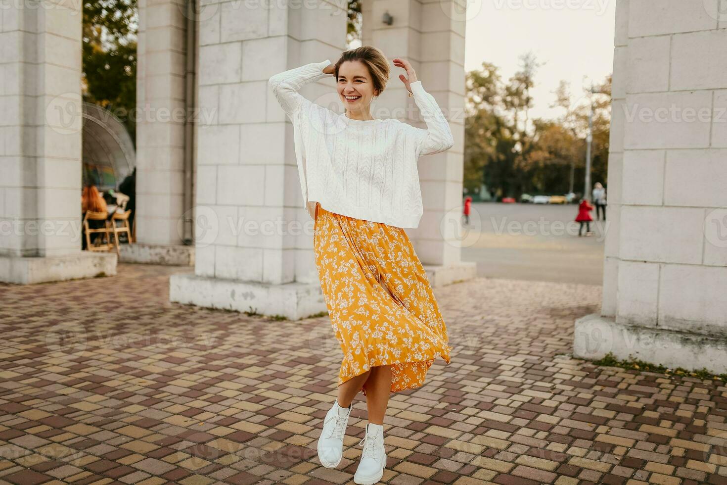 young pretty happy smiling woman in yellow printed dress and knitted white sweater photo