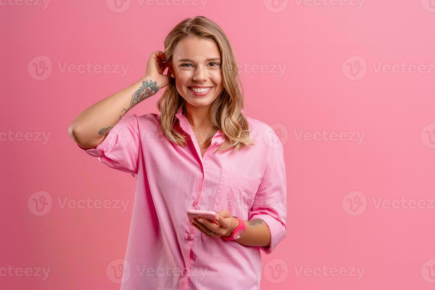 blond pretty woman in pink shirt smiling holding holding using smartphone photo