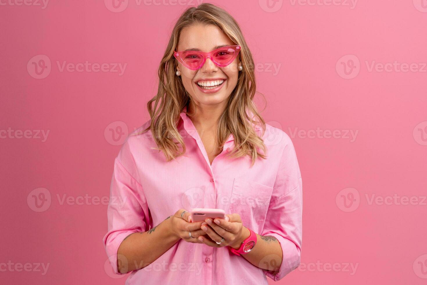 blond pretty woman in pink shirt smiling holding holding using smartphone photo