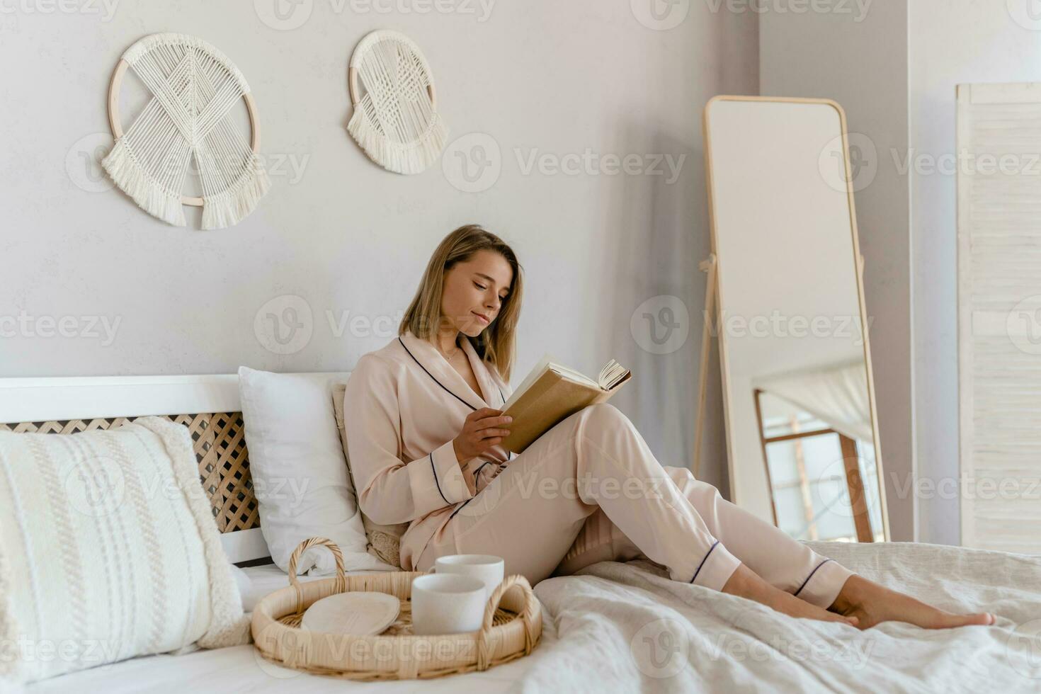 pretty smiling woman relaxing at home on bed in morning in pajamas reading book photo
