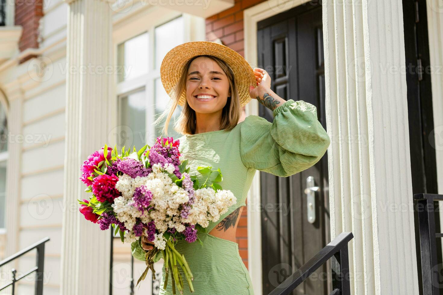 beautiful young woman in summer style outfit smiling happy walking with flowers in city street photo