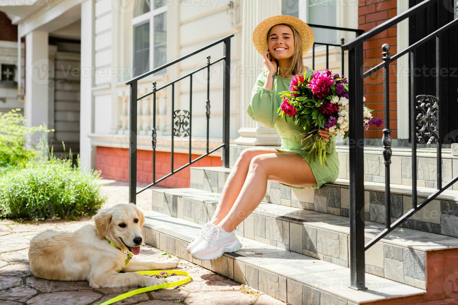 beautiful young woman in summer style outfit smiling happy walking with flowers and dog photo