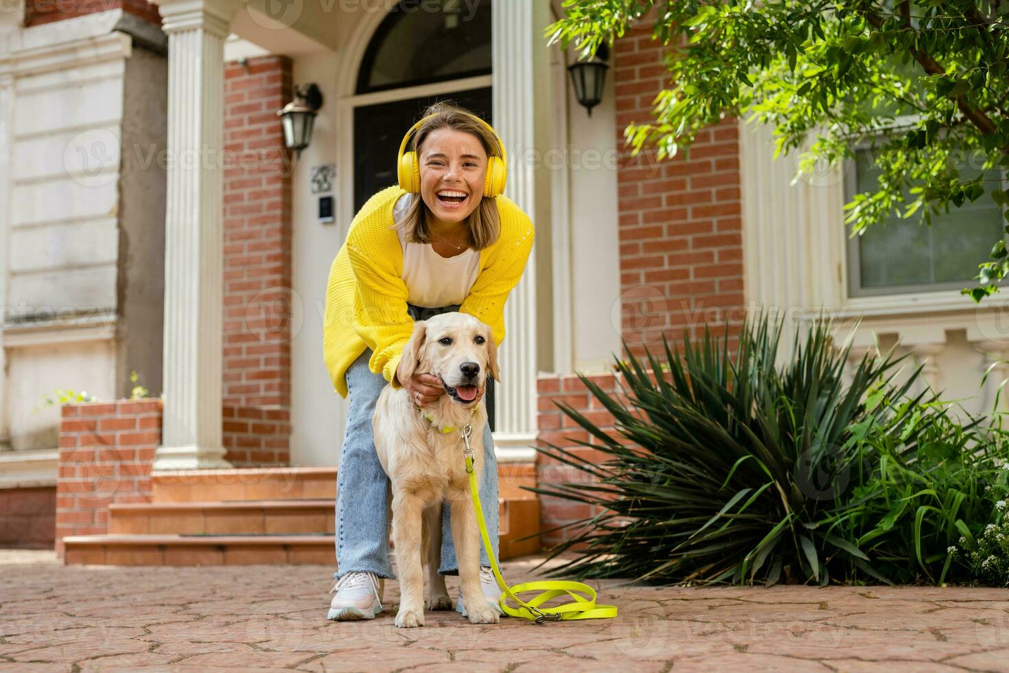 woman in yellow sweater walking at her house with a dog listening to music in headphones photo