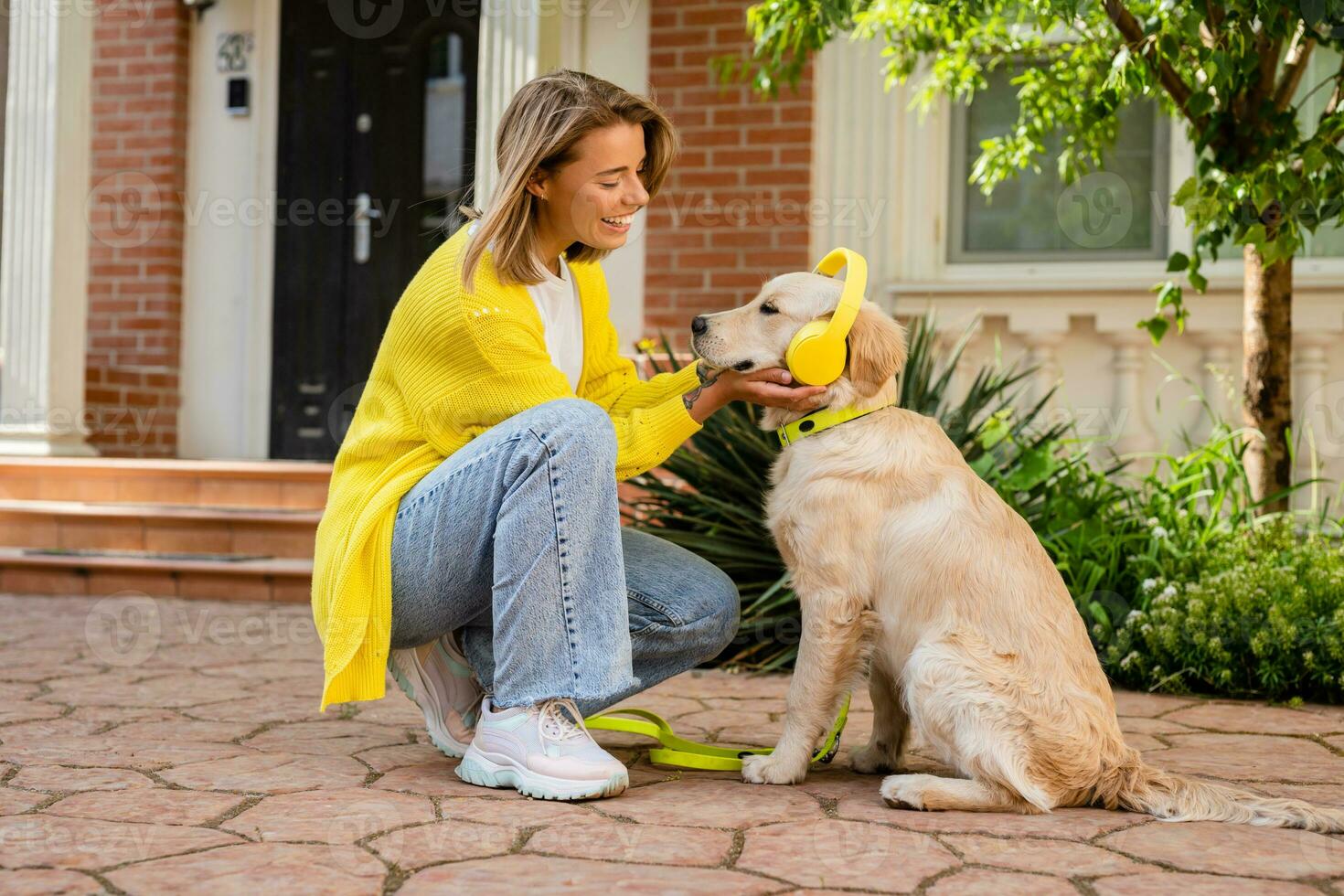 woman in yellow sweater walking at her house with a dog listening to music in headphones photo