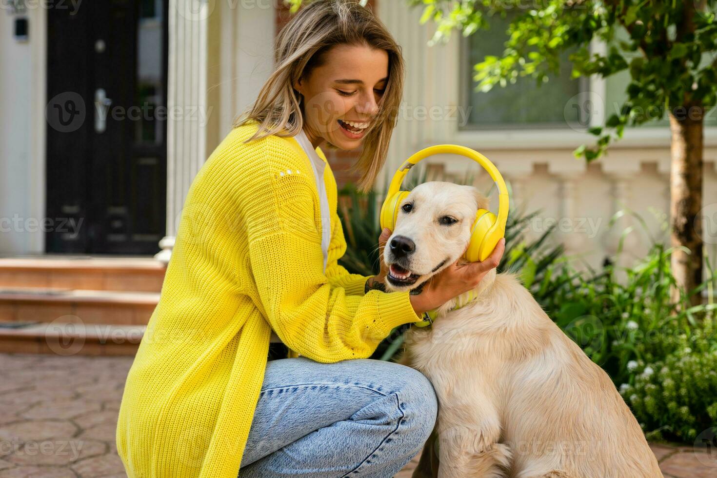 woman in yellow sweater walking at her house with a dog listening to music in headphones photo