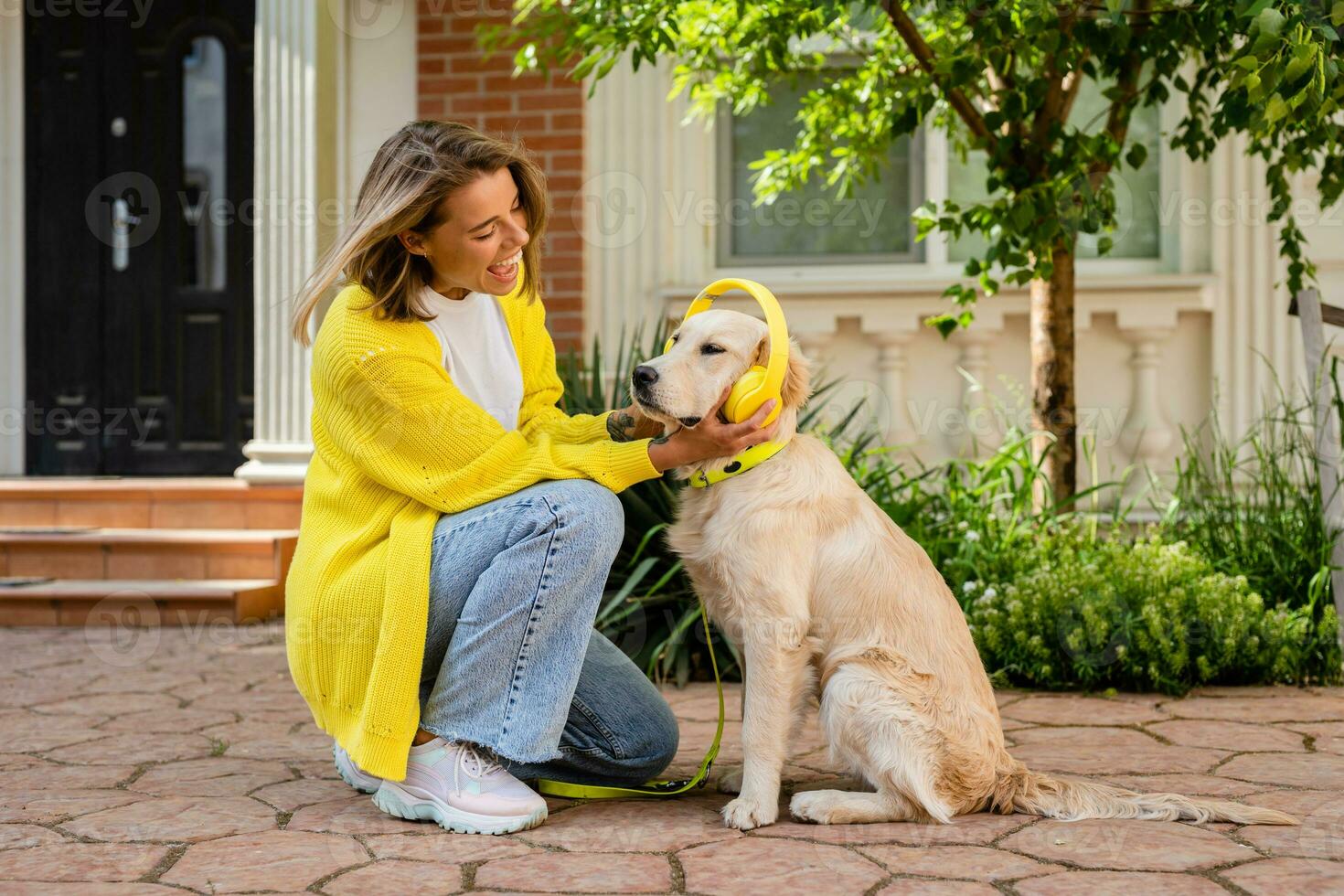 woman in yellow sweater walking at her house with a dog listening to music in headphones photo