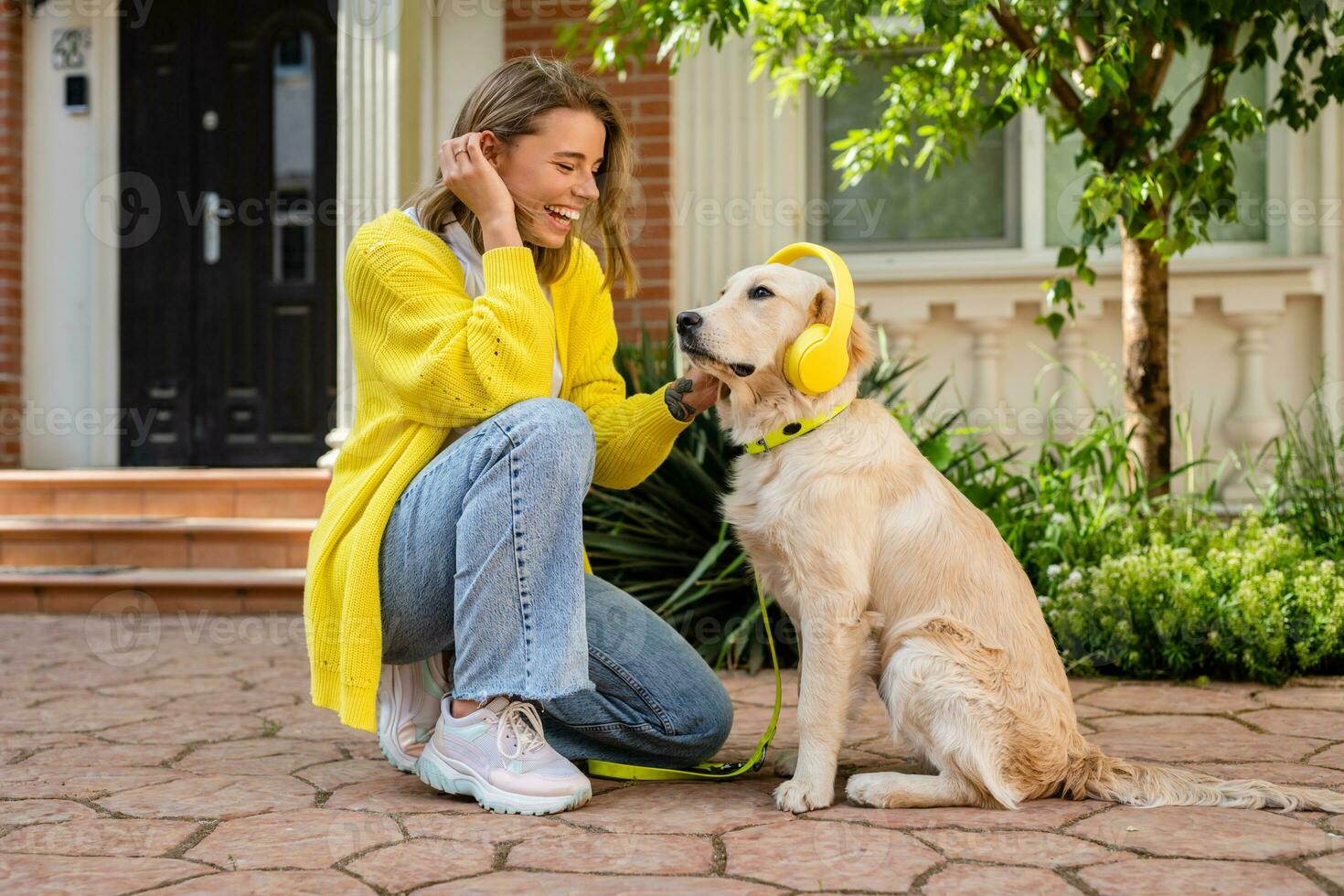 woman in yellow sweater walking at her house with a dog listening to music in headphones photo