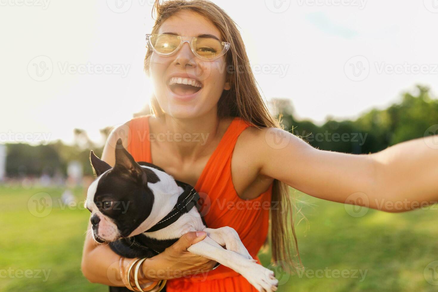 young happy smiling woman in orange dress having fun playing with dog in park photo