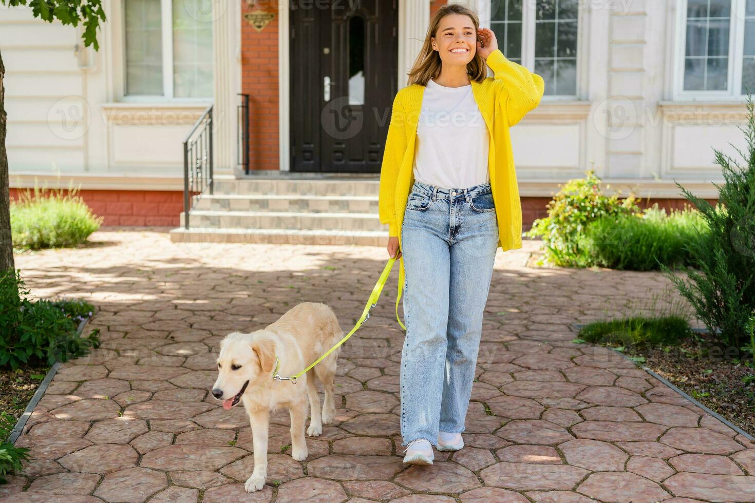 happy smiling woman in yellow sweater walking at her house with a dog golden retriever photo