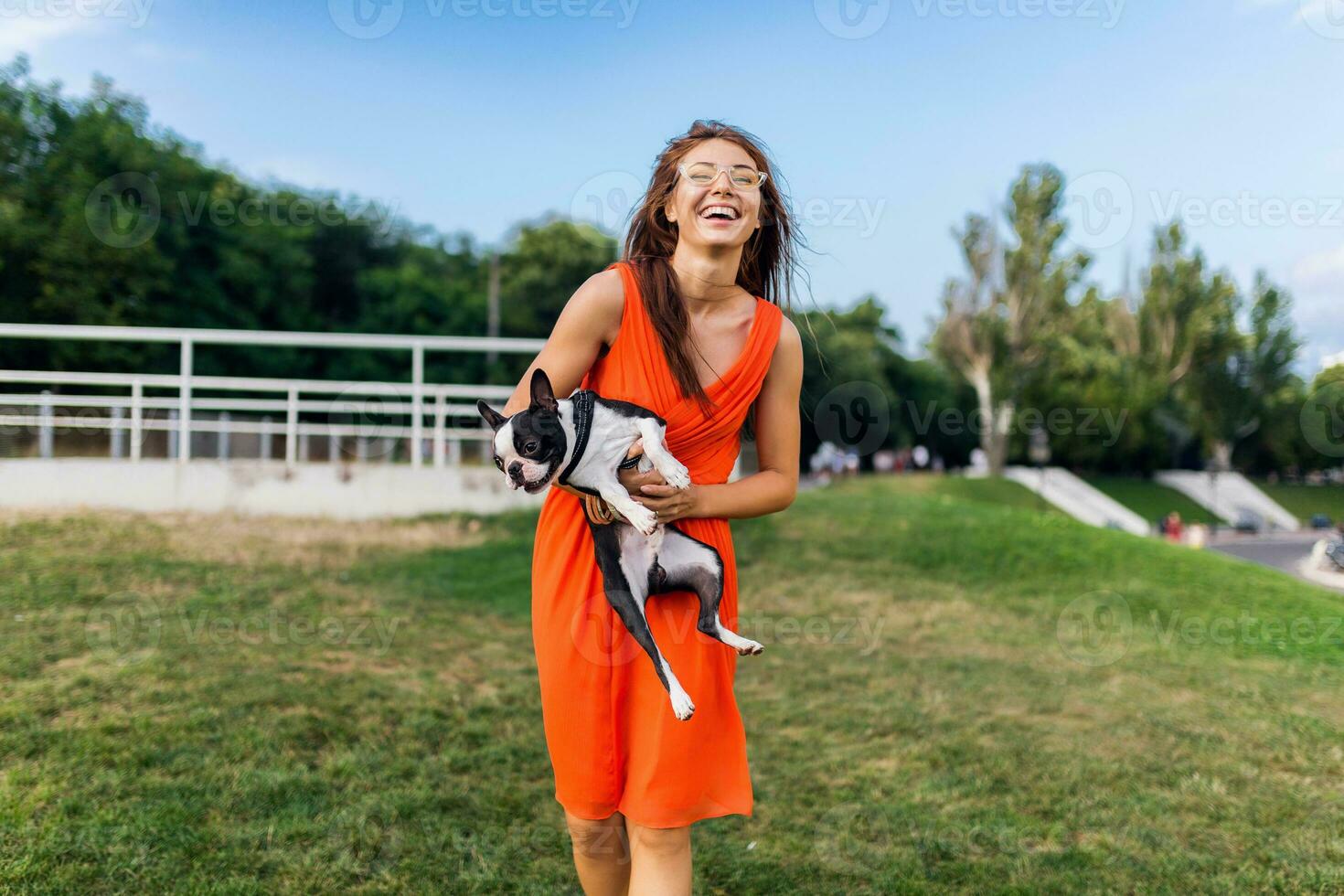young happy smiling woman in orange dress having fun playing with dog in park photo