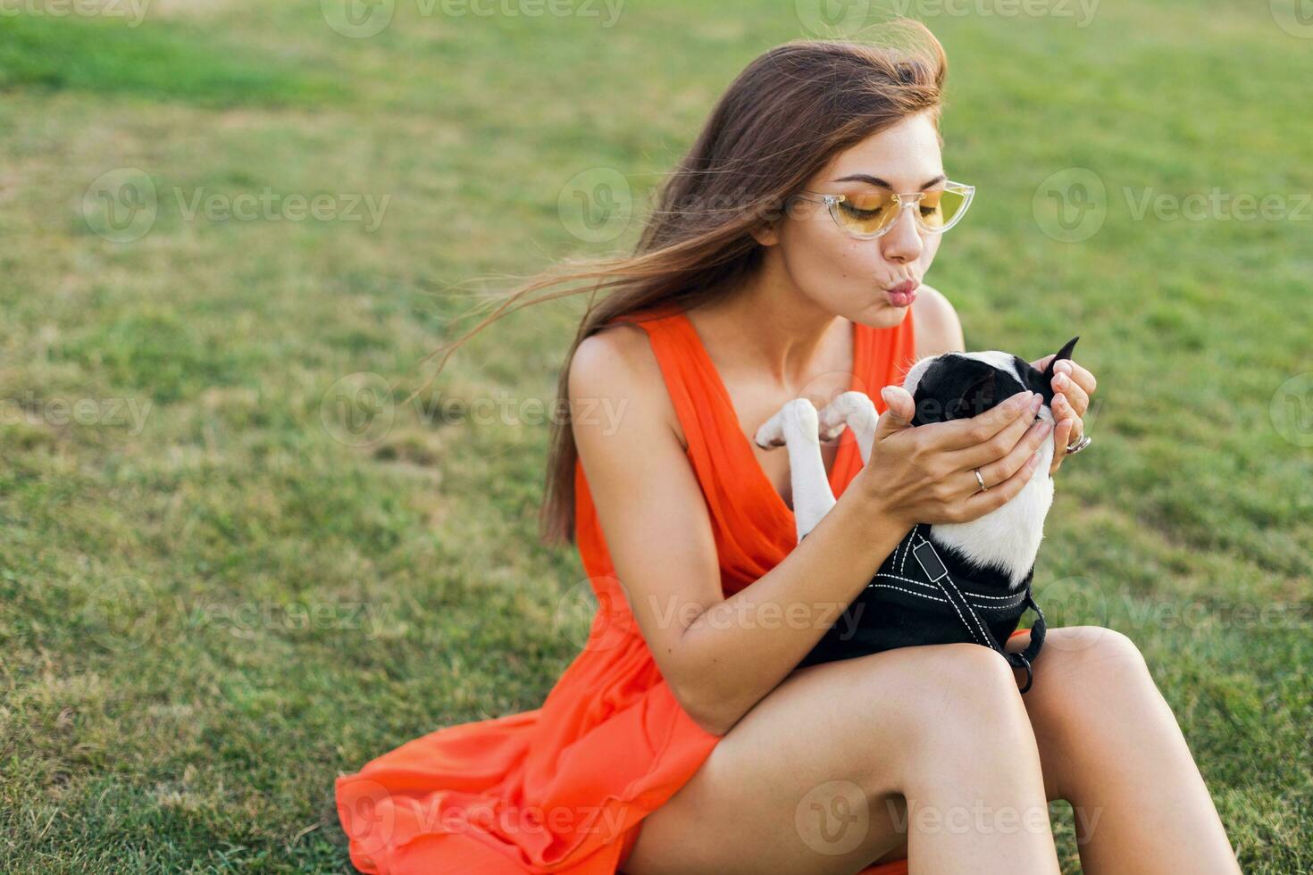 young happy smiling woman in orange dress having fun playing with dog in park photo