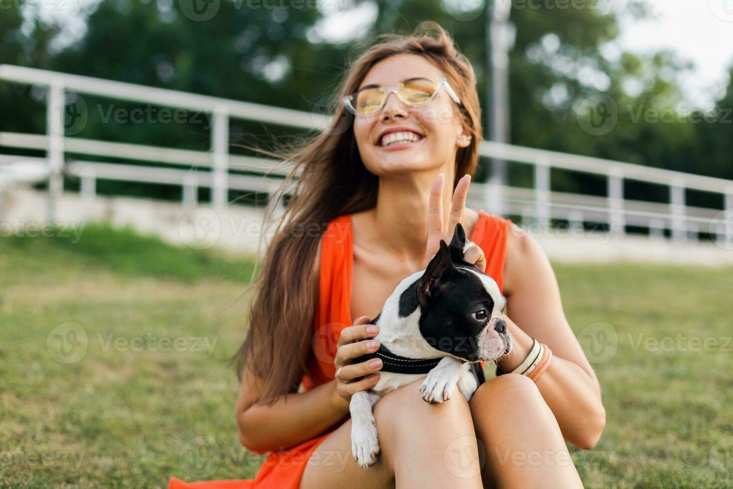 young happy smiling woman in orange dress having fun playing with dog in park photo