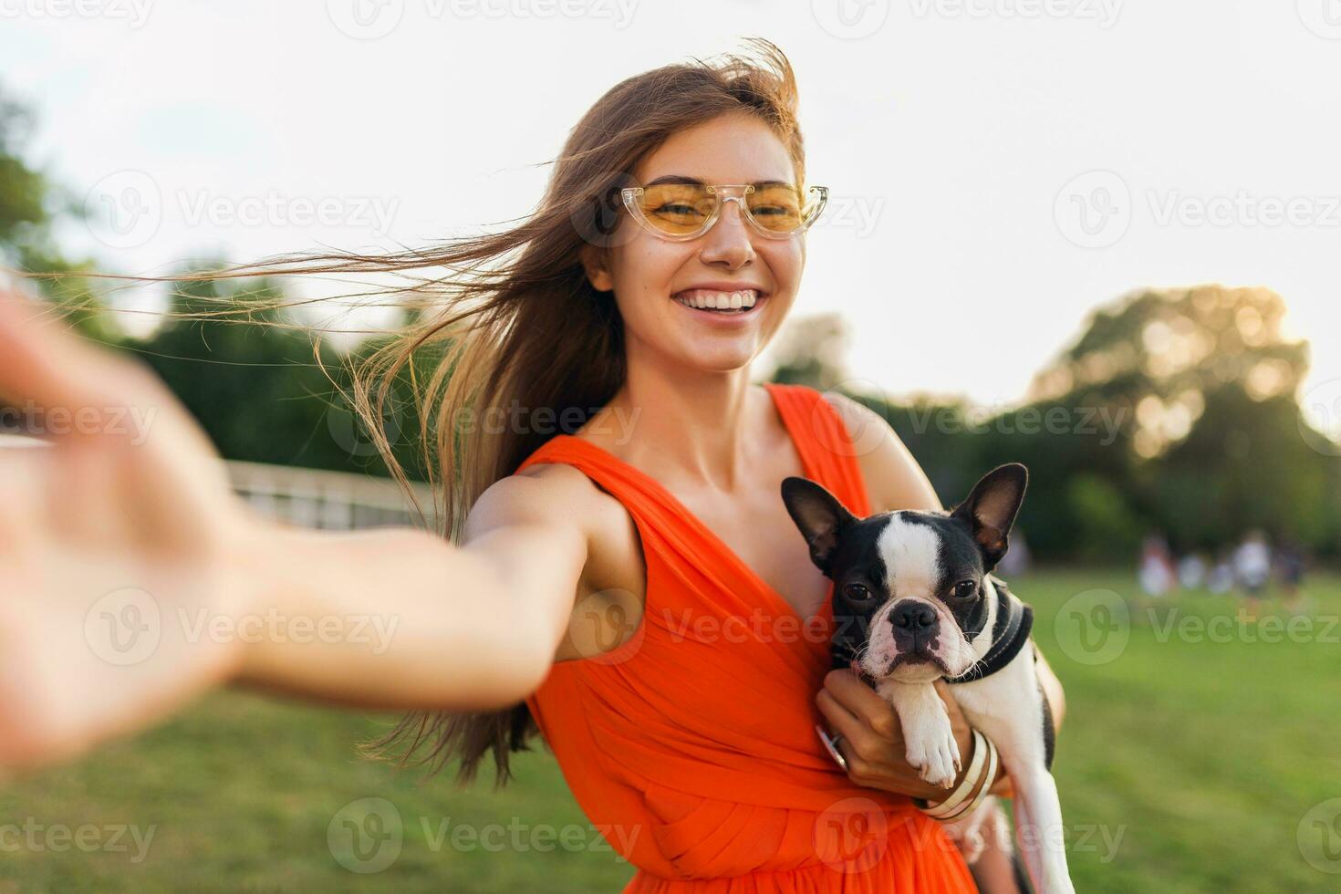 young happy smiling woman in orange dress having fun playing with dog in park photo