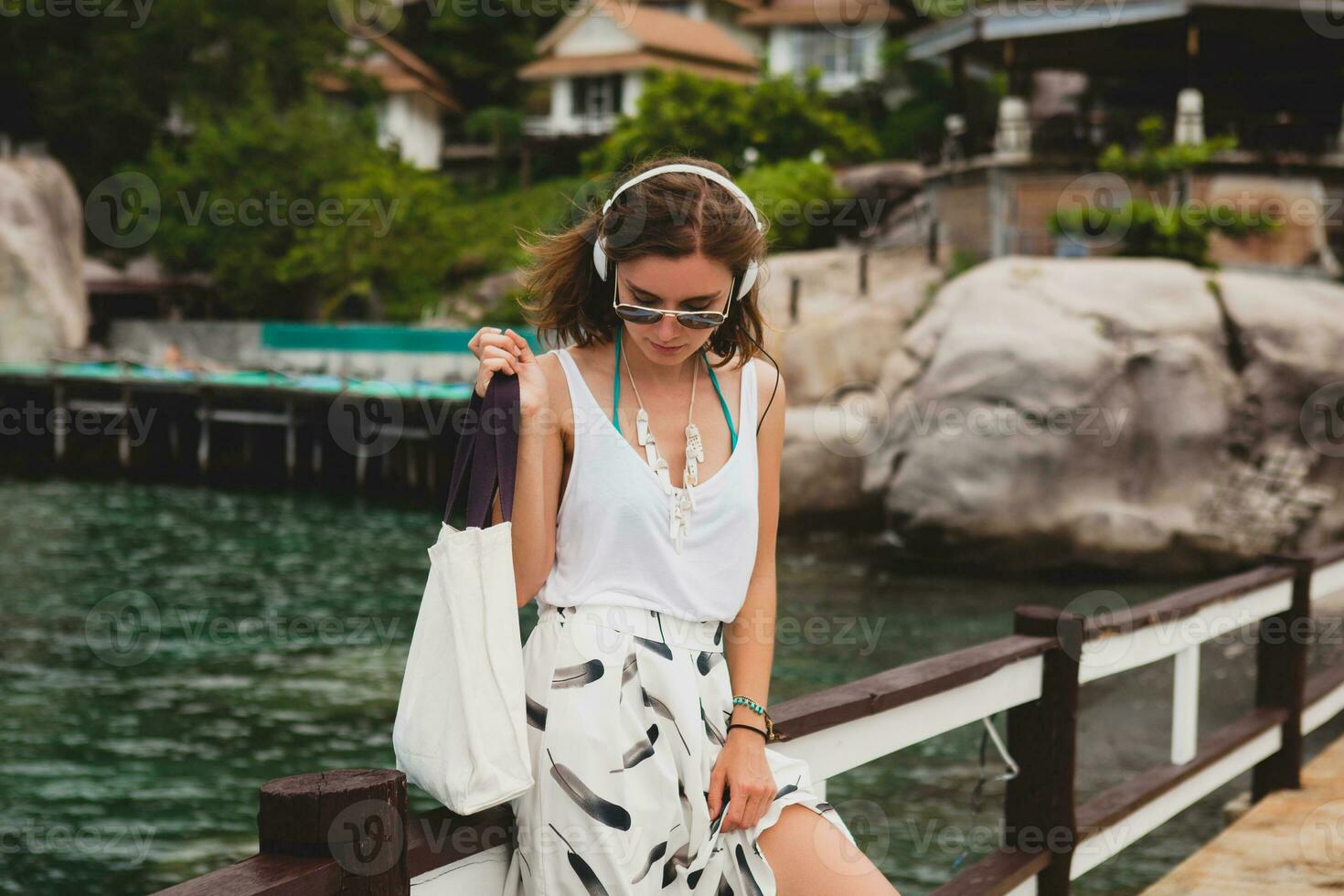 young stylish woman standing on pier, walking, listening to music photo