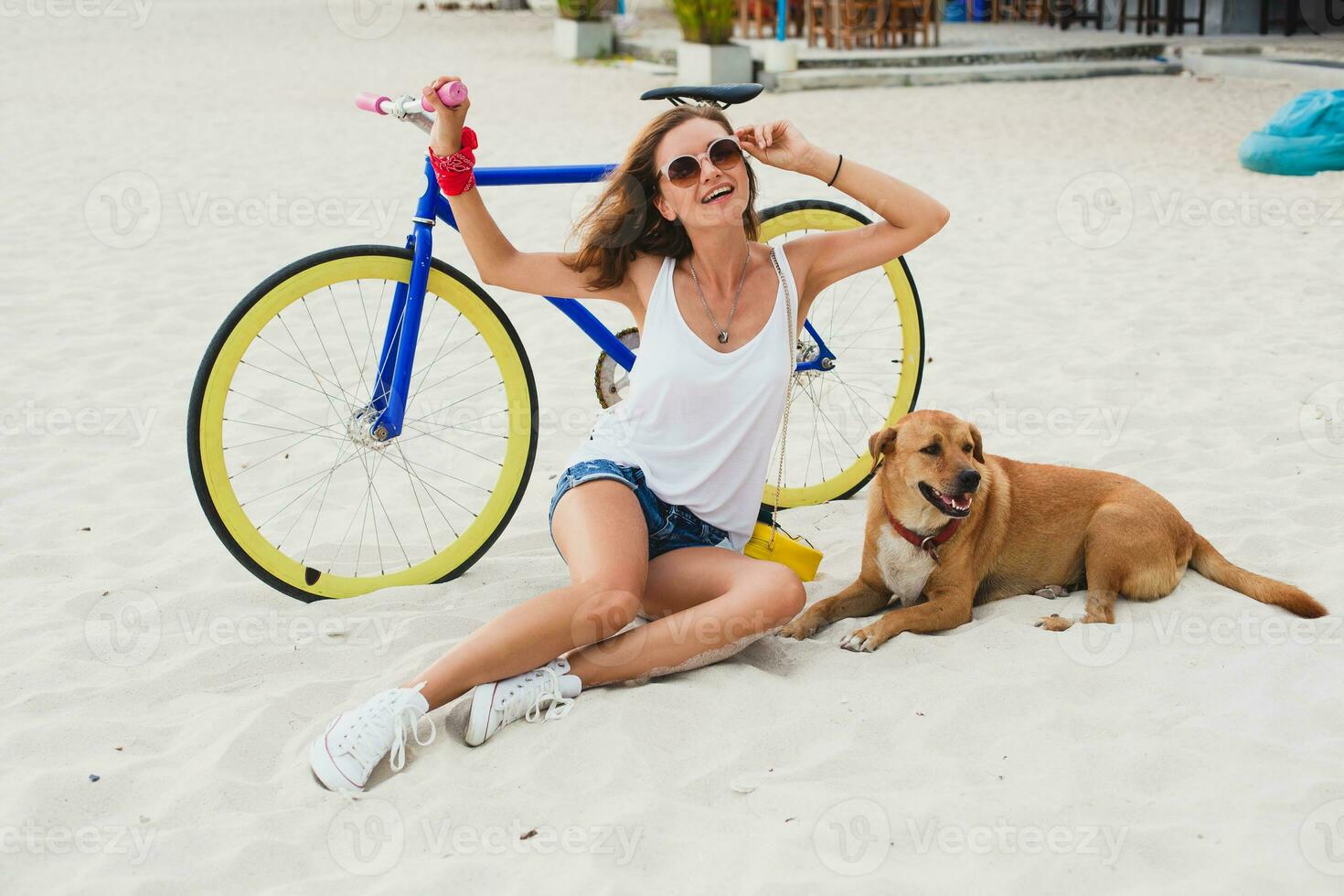 young beautiful woman sitting on sand on beach, holding vintage bicycle photo