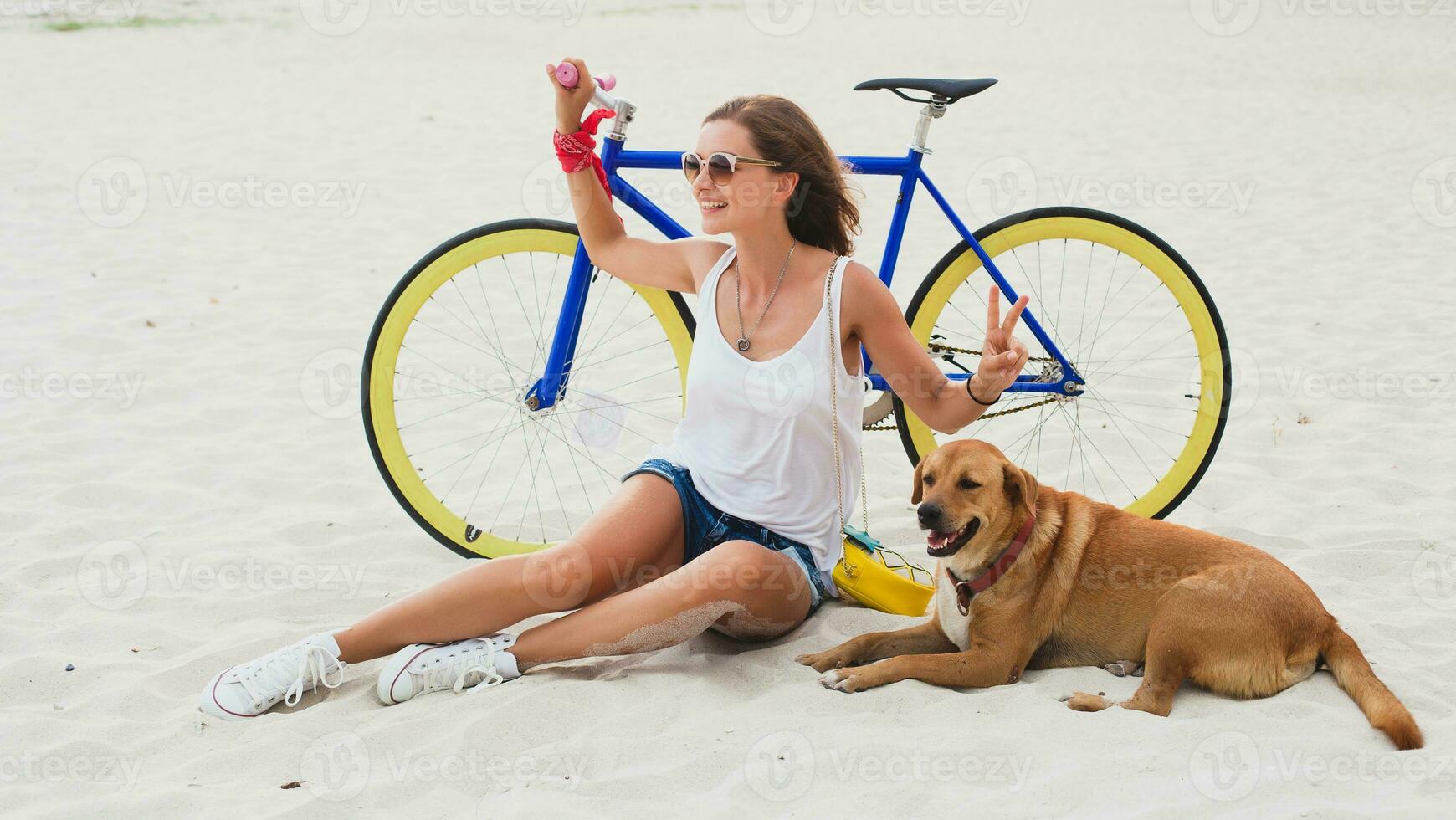 young beautiful woman sitting on sand on beach, holding vintage bicycle photo