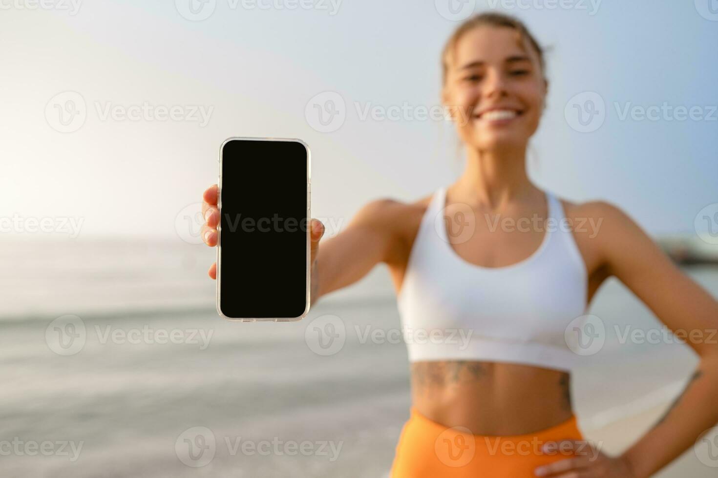 pretty young smiling woman doing sports in the morning in stylish sport outfit sportswear, holding smartphone screen close-up photo