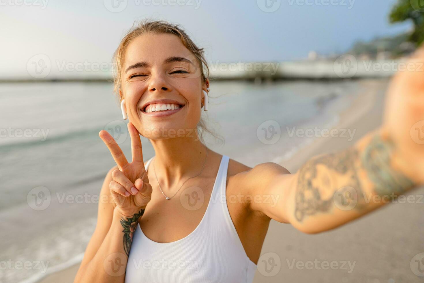 bonito joven sonriente mujer haciendo Deportes en el Mañana en elegante deporte atuendo ropa de deporte, tomando selfie imagen en teléfono inteligente cámara foto