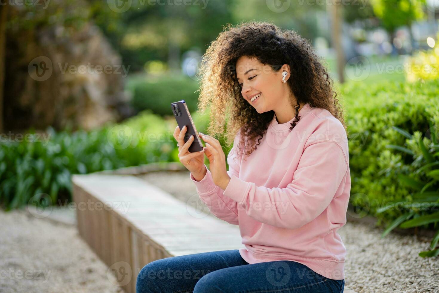 pretty beautiful curly young woman sitting in park using smatphone photo