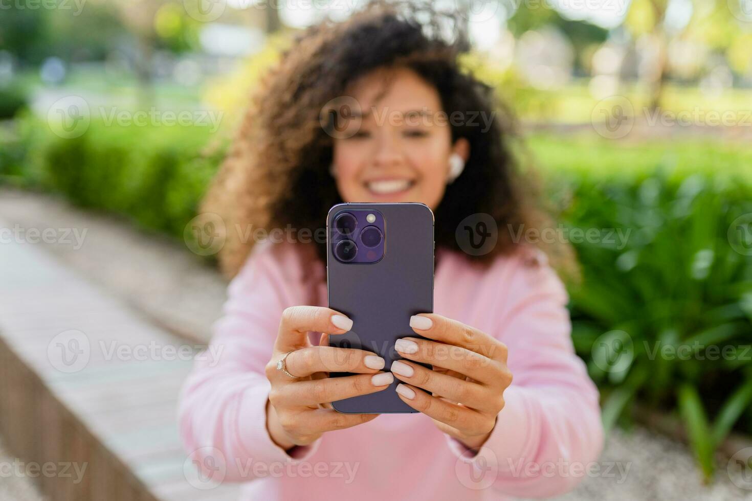 pretty beautiful curly young woman sitting in park using smatphone photo