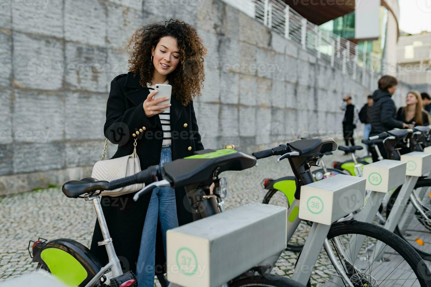 pretty curly woman renting a bicycle in street with an app photo