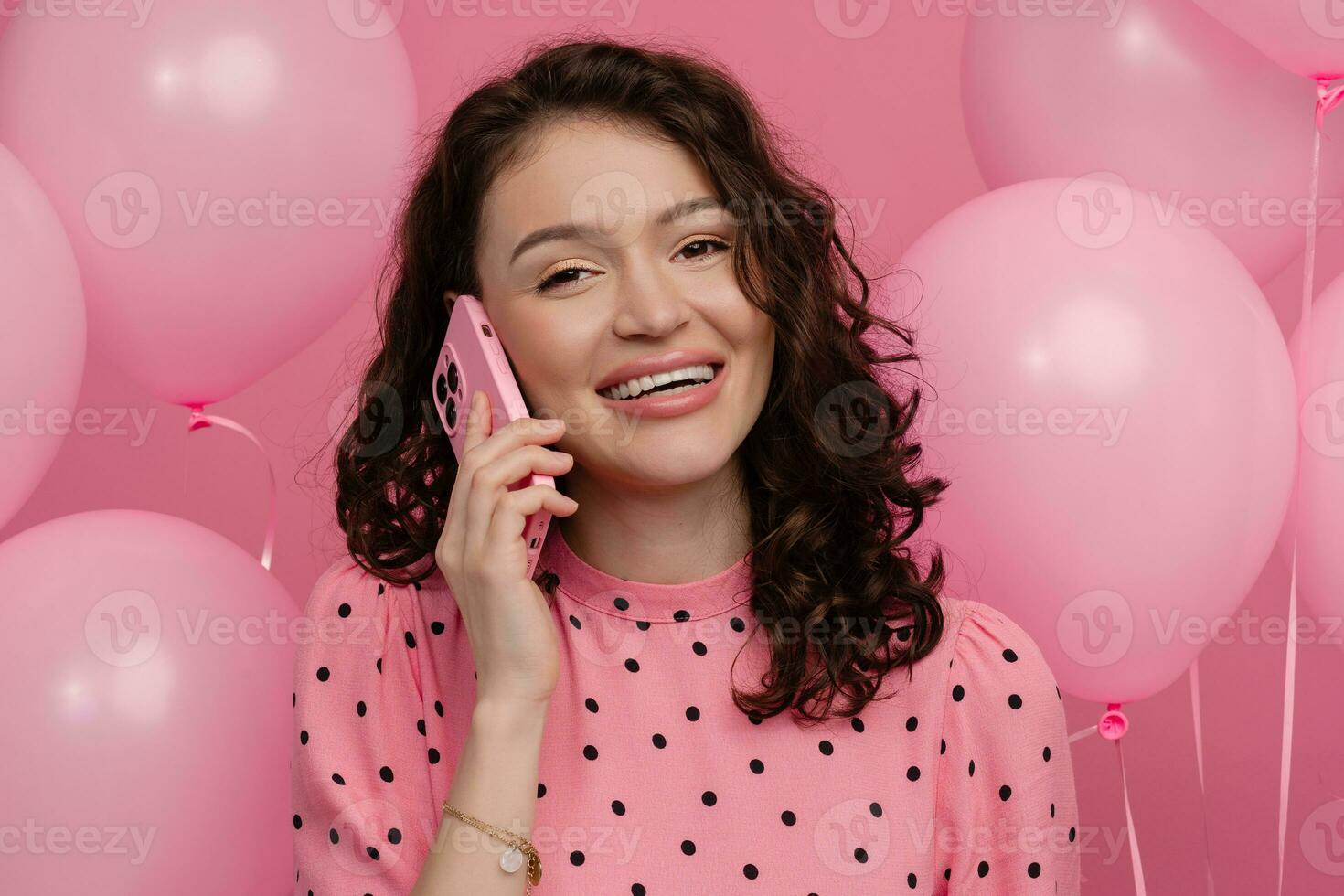 pretty young woman posing isolated on pink studio background with pink air baloons and smartphone photo