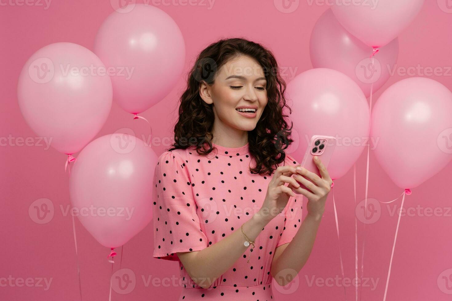 pretty young woman posing isolated on pink studio background with pink air baloons and smartphone photo