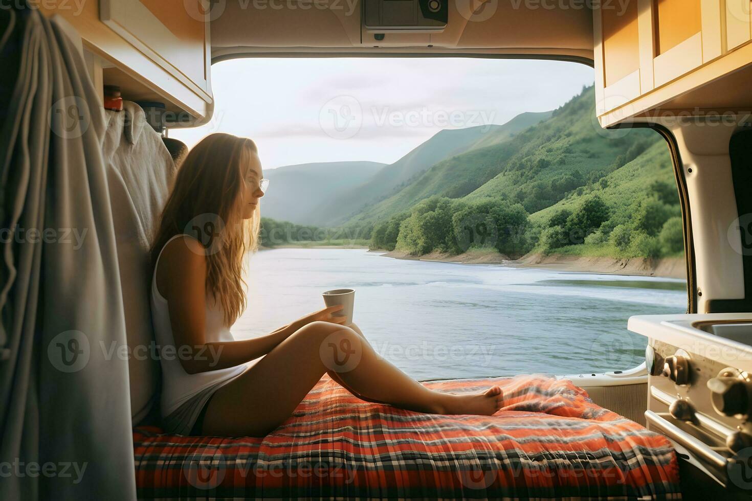 Camper girl holding coffee cup inside camper van at riverside. photo